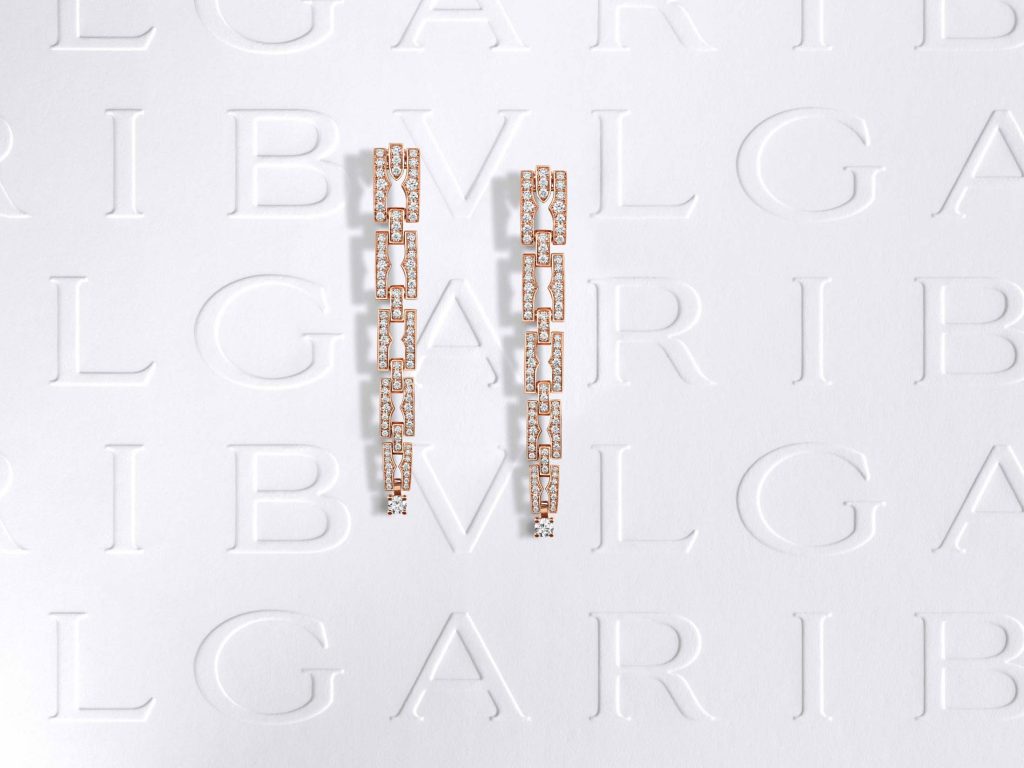 Two vertical bars of Bulgari's signature rose gold and diamond-studded bracelets, aligned against a white backdrop with a prominent embossed Bulgari logo, exemplifying the brand's timeless design and luxurious allure.