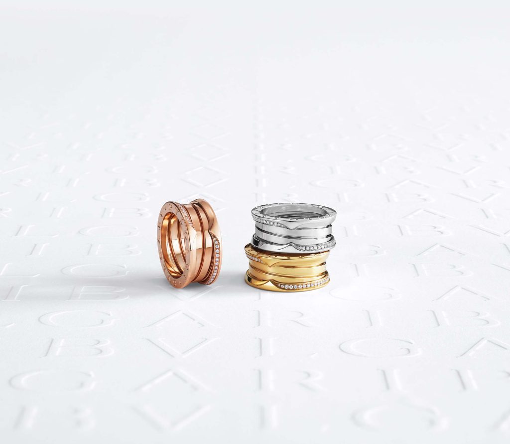 A balanced composition of Bulgari's B.zero1 rings in rose gold, silver, and yellow gold, some adorned with diamonds, on a pristine background with a delicately embossed logo, embodying the harmonious blend of innovation and tradition.