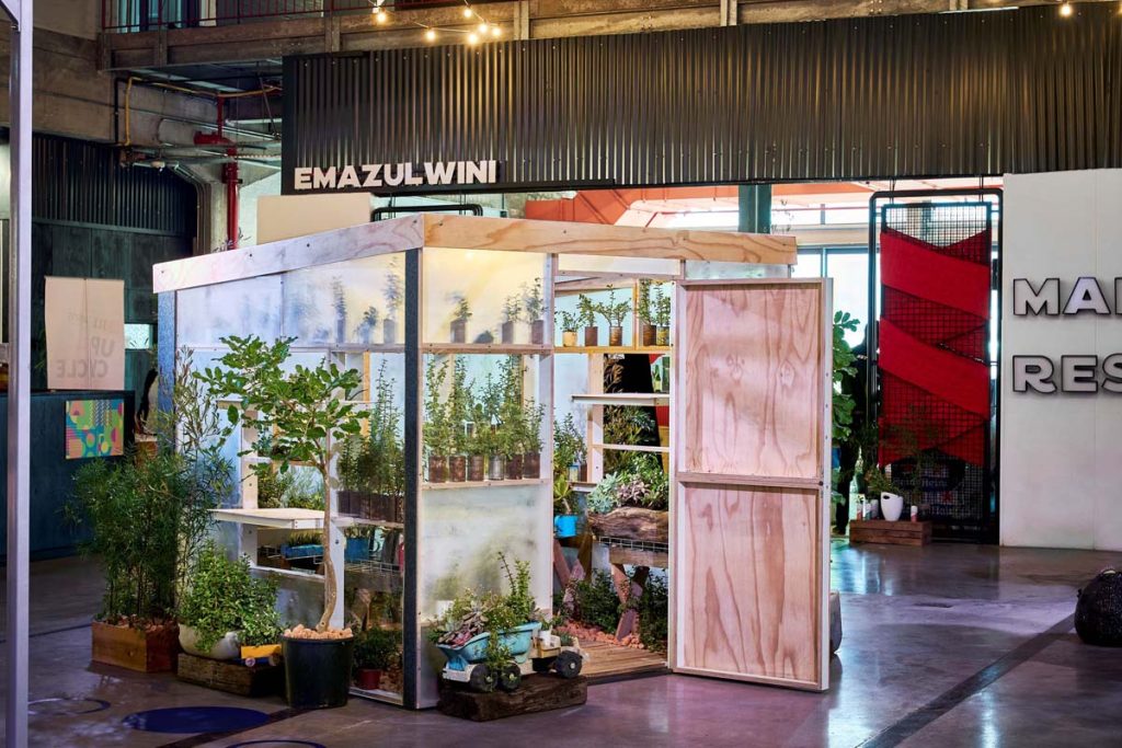 The UPCYCLE Oxygen Farm Work Pod, showcasing a transparent cabin filled with lush greenery, highlighting innovative repurposing of office furniture.