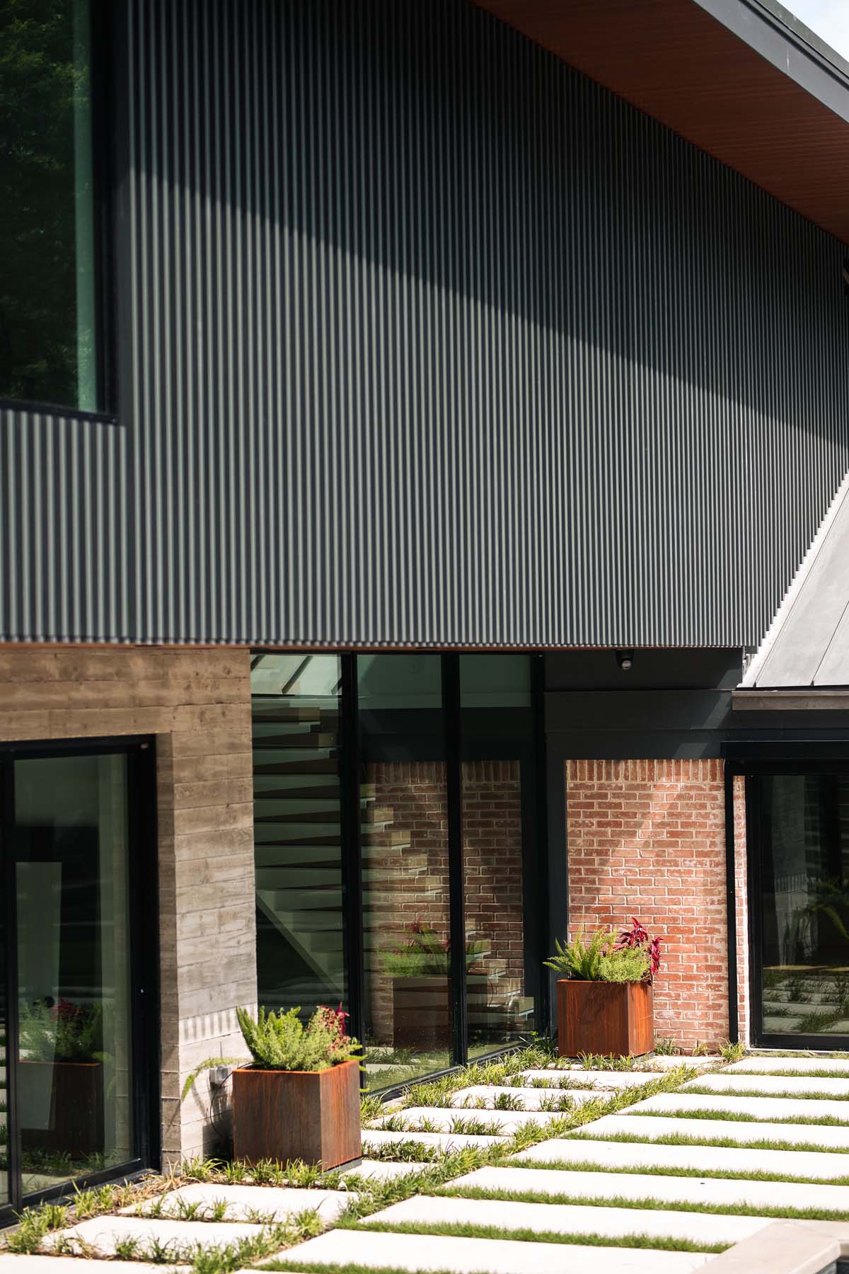 Detailed view of Dissonant House’s textured facade featuring aluminum battens, natural stone elements, and greenery-filled planters, highlighting the blend of modern design with organic touches.