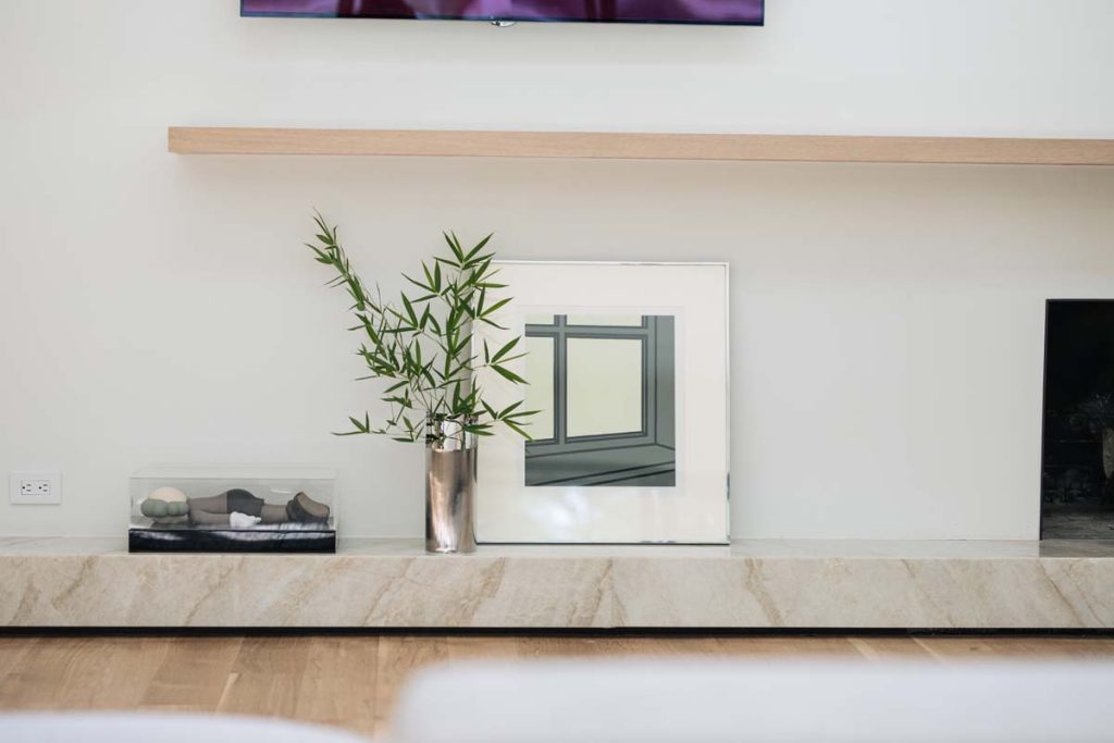 Minimalist living space in Dissonant House featuring a modern fireplace with a sleek wooden mantel, framed artwork, and a natural stone base, blending heritage and contemporary design.