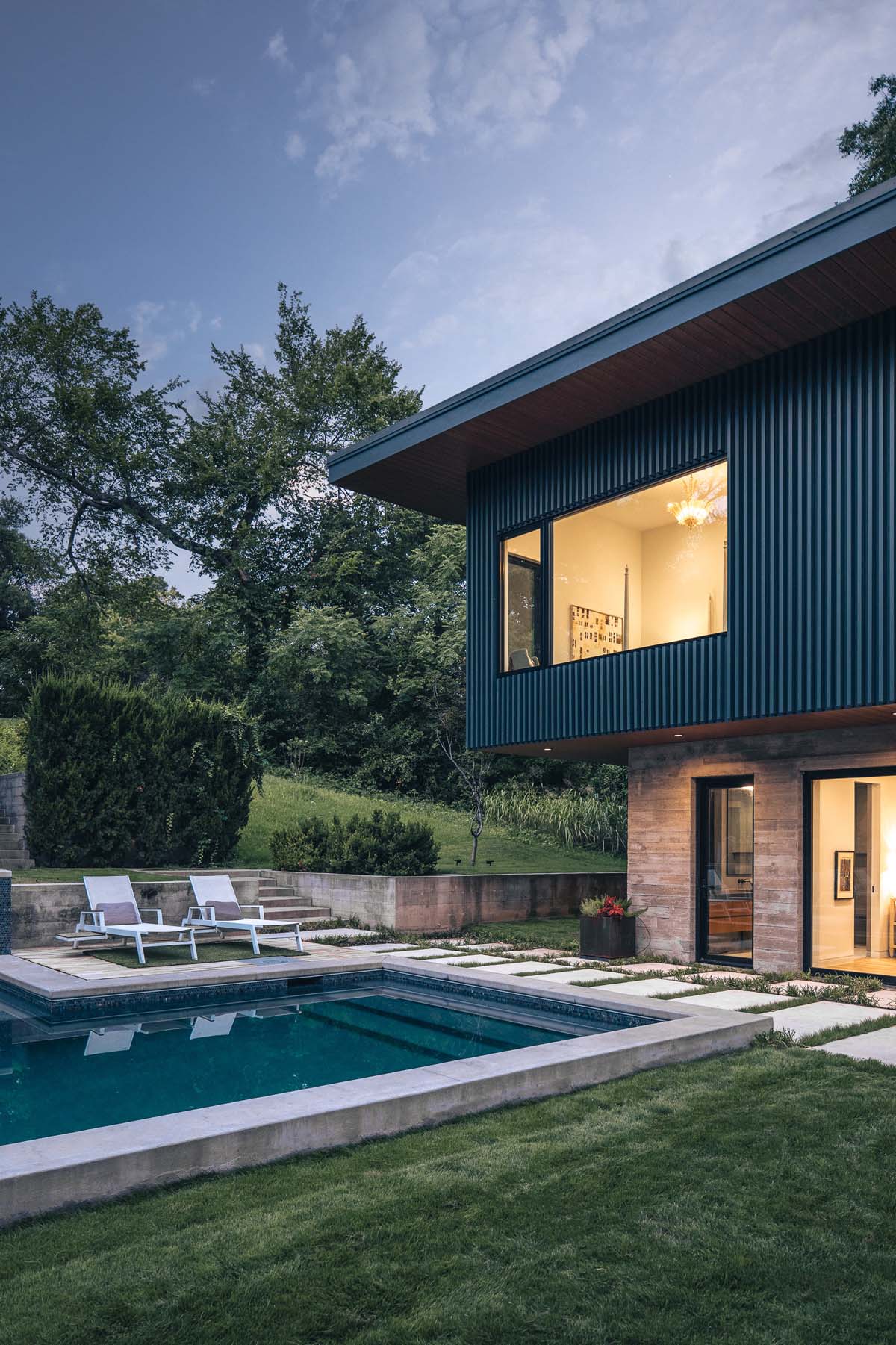 Poolside view of Dissonant House with a modern lounge area and large windows that invite natural light into the living spaces, creating a serene and stylish outdoor retreat.