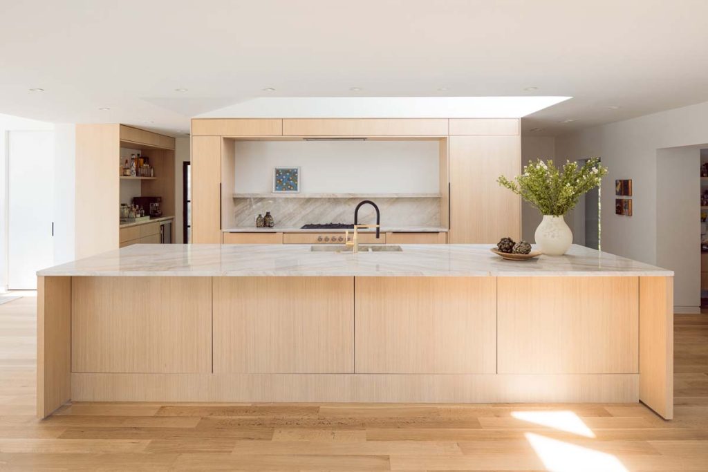 Contemporary kitchen in Dissonant House featuring a natural stone backsplash, minimalist cabinetry, and framed artwork, blending modern aesthetics with artistic touches and luxury finishes.