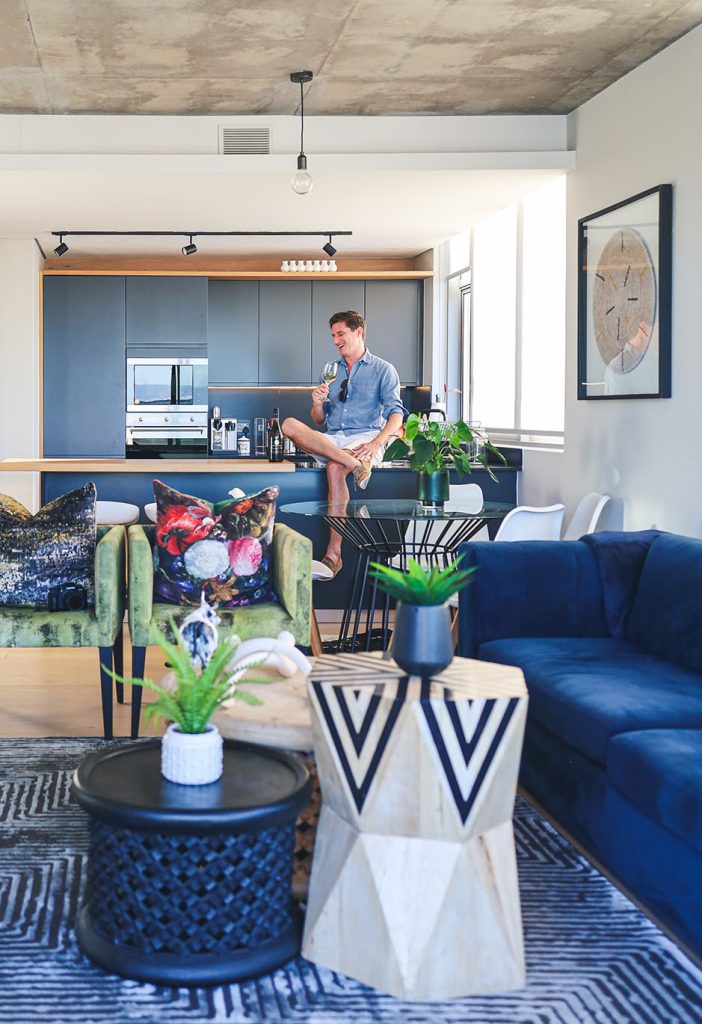 Stylishly designed Cape Town holiday rental with blue cabinetry, velvet chairs, and layered textures showcasing refined interior design.