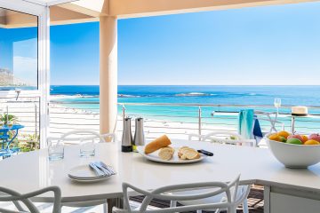 Modern dining area in a Cape Town beachfront holiday rental with ocean view, white furniture, and bright coastal interior design.