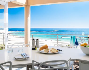 Modern dining area in a Cape Town beachfront holiday rental with ocean view, white furniture, and bright coastal interior design.
