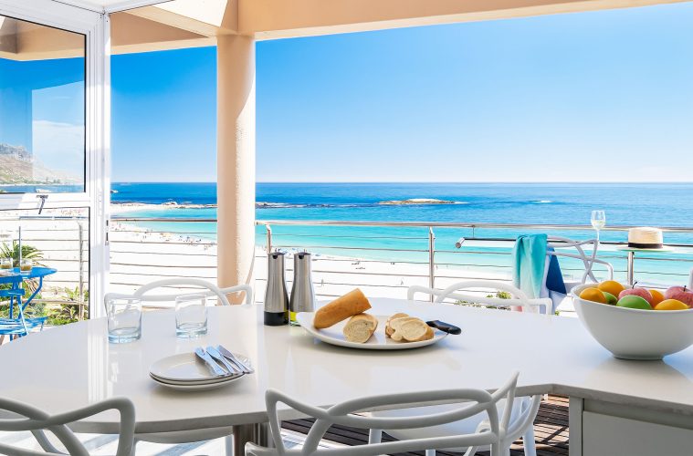 Modern dining area in a Cape Town beachfront holiday rental with ocean view, white furniture, and bright coastal interior design.