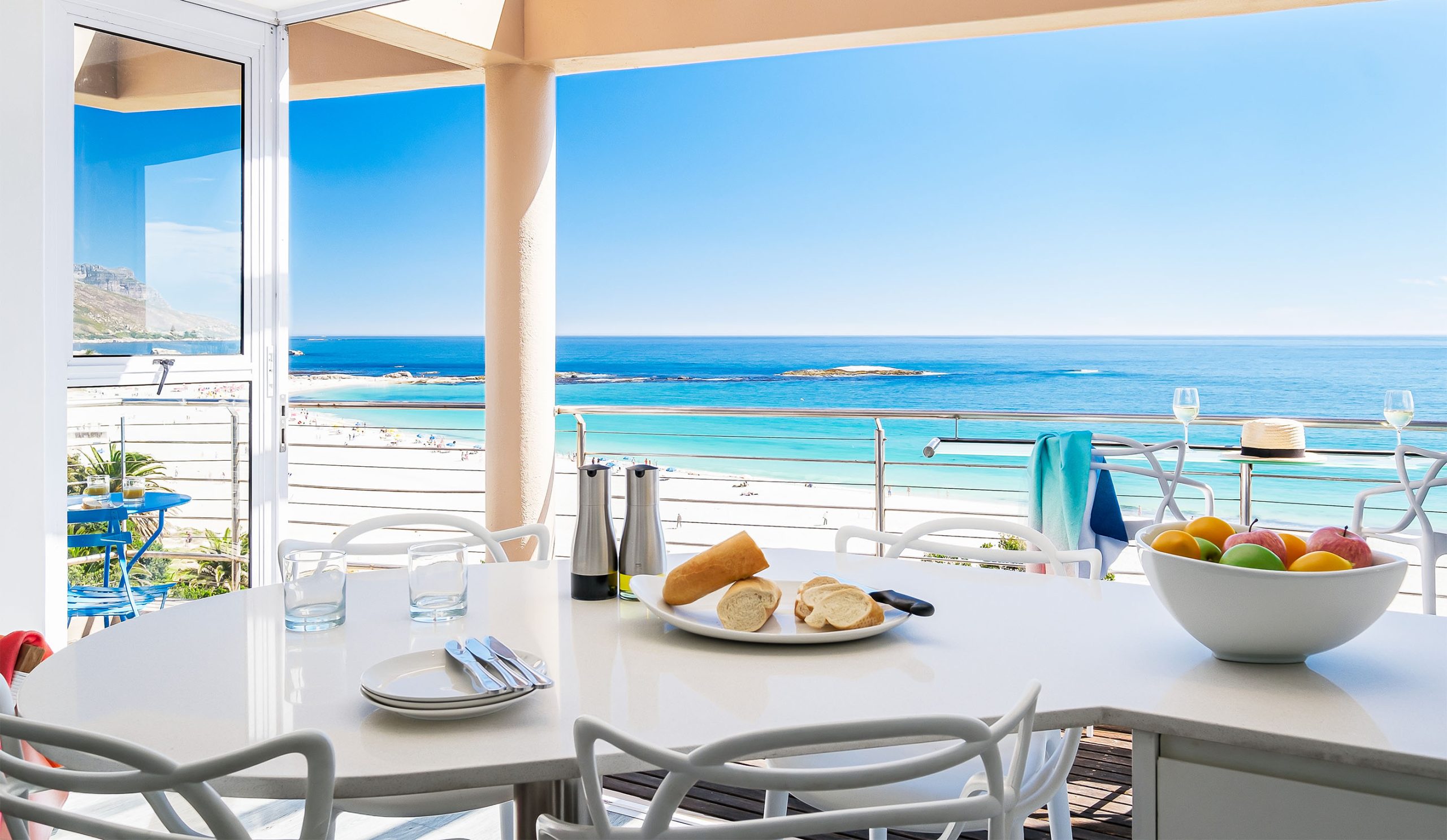 Modern dining area in a Cape Town beachfront holiday rental with ocean view, white furniture, and bright coastal interior design.